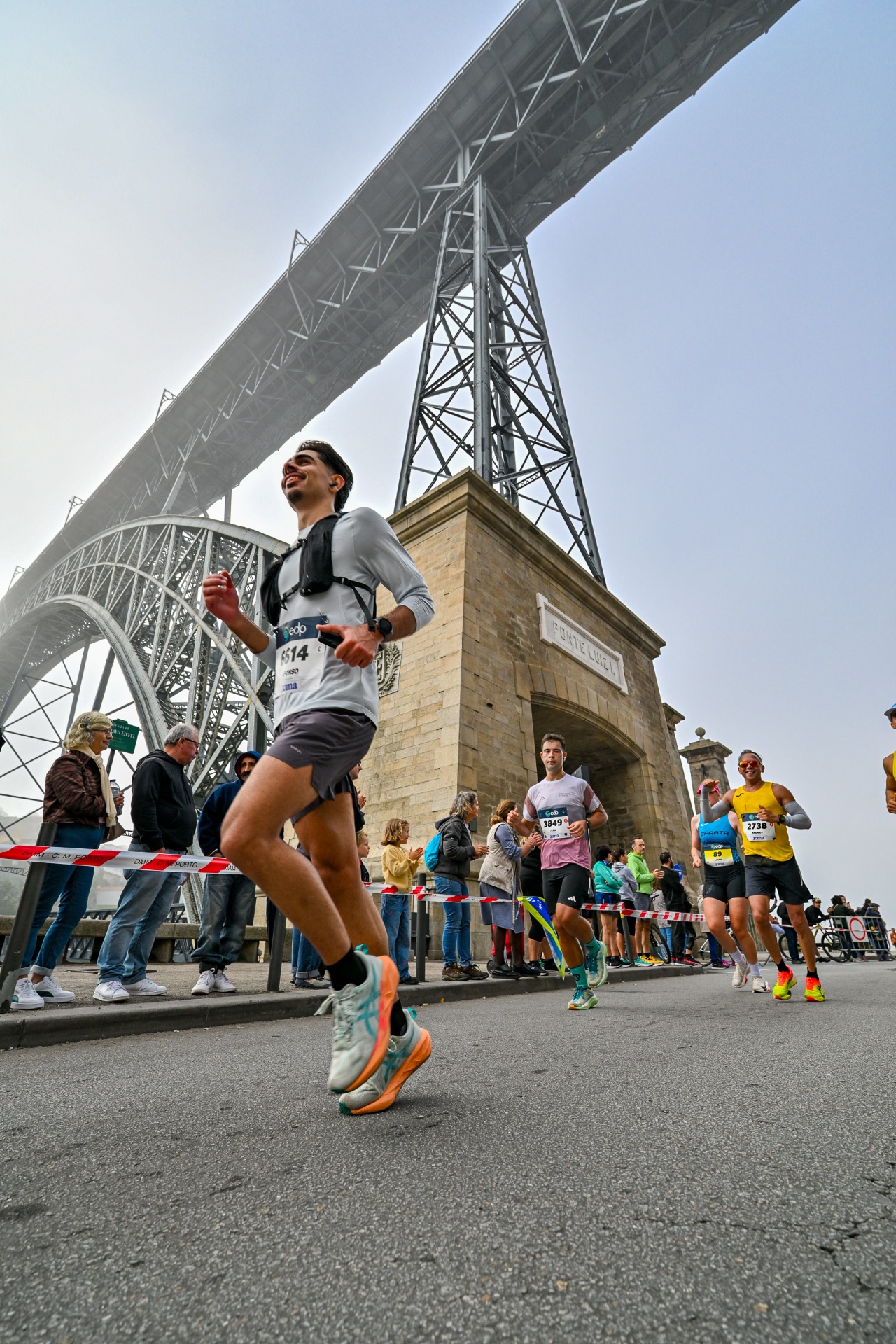 Afonso a correr a sorrir sob a Ponte Luiz I com o dorsal 6614 da Maratona EDP do Porto